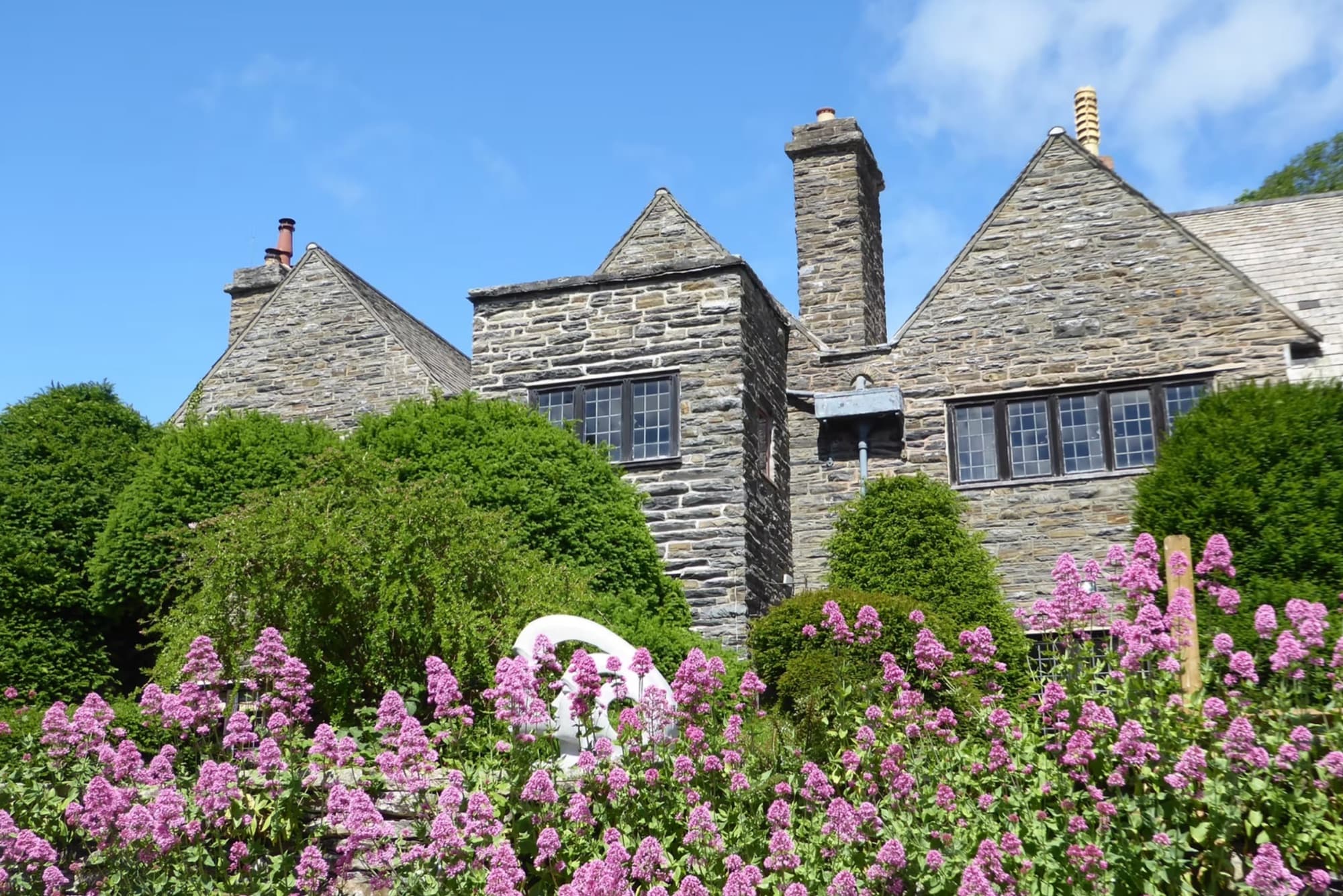 Tan-y-Garth Hall's stone gables rising above a bank of pink valerian