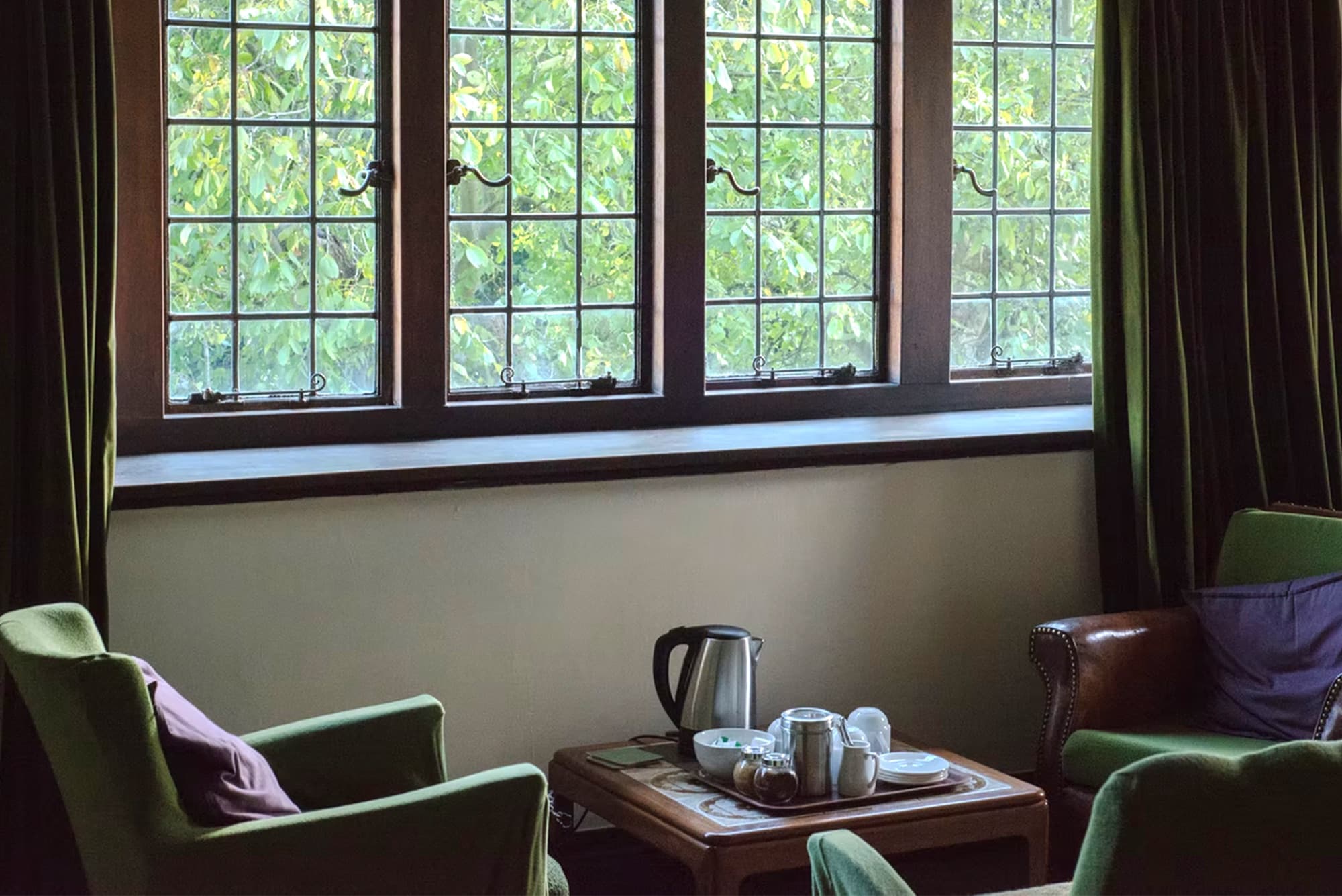 Armchairs and a tea tray beside leaded windows looking onto trees